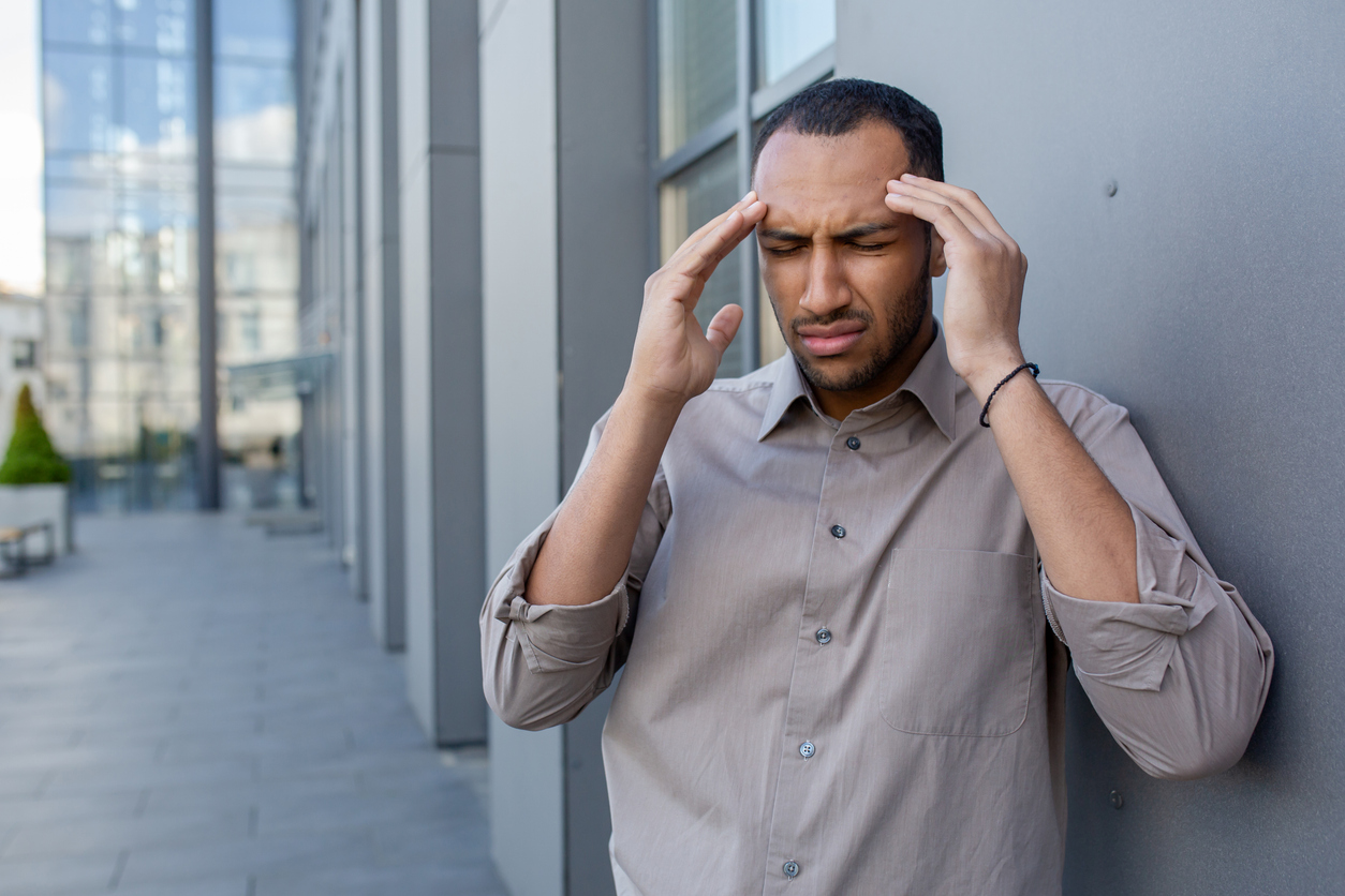 sick-diverse-male-suffering-from-severe-headache-and-rubbing-forehead-while-standing-by-wall-outdoors-tired-exhausted-man-feeling-unexpected-dizziness-and-struggling-with-high-blood-pressure